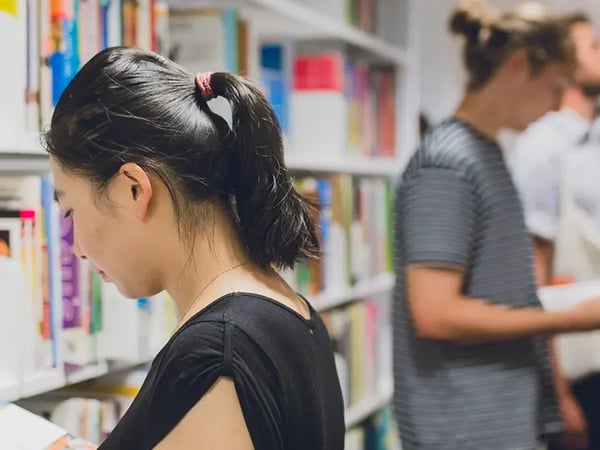 Students perusing books in a library shelf aisle