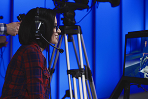 Woman wearing a headset sitting behind a monitor with the cameraman during production